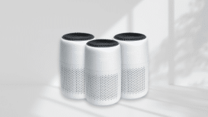 Three white cylindrical air purifiers with black tops are arranged in a row against a light background with soft shadows.