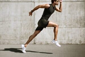 Man in athletic attire running outdoors against a concrete wall background.