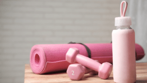 Pink fitness set with a yoga mat, two 2-pound dumbbells, and a water bottle, all arranged on a wooden surface.
