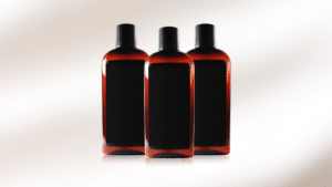 Three amber-colored bottles with black labels and black caps are arranged side by side, creating a uniform and stylish look against a softly lit background.