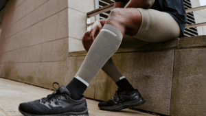 Man wearing compression socks and black athletic shoes, sitting on an outdoor ledge, ready for a workout or recovery session.