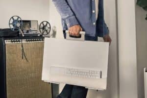 Person carrying a sleek, portable desktop computer with an integrated keyboard, standing near audio equipment.